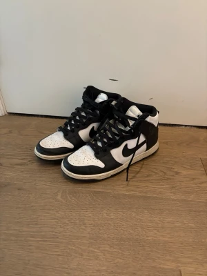 Nike Dunk High Panda sneakers - Säljer ett par Nike Dunk High Panda sneakers i svart och vitt läder. Klassisk hög siluett med svart swoosh, svarta skosnören och vit tåbox. Perfekta för dig som gillar streetwear och vill ha en tidlös look. OBS! PRIS KAN DISKUTERAS 