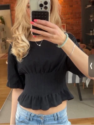 Svart croppad topp med volang  - Säljer en svart croppad topp med lite peplum liknade vid magen. Den är i storlek m men passar som en s. Perfekt till sommaren 