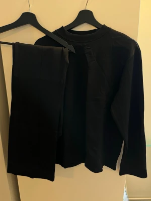 Chimi Svart set med långärmad topp och byxa - Säljer ett svart set med långärmad topp och matchande byxa. Setet har enkel design med raka linjer och är gjort i ett slätt material som känns mjukt mot huden. Perfekt för dig som gillar minimalistisk stil och vill ha något bekvämt.  Tröja S byxa M