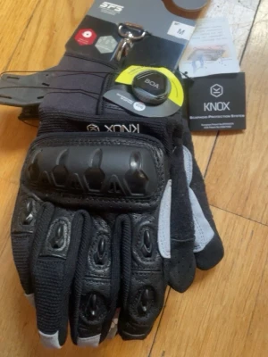 Svarta Knox motorcykelhandskar - Säljer ett par svarta motorcykelhandskar från Knox med skyddande paneler på ovansidan och detaljer i grått. Handskarna har BOA-spänne och är tillverkade i skinn och syntetmaterial för extra slitstyrka och komfort. Perfekta för dig som vill ha både stil och säkerhet på vägen. De är även helt nya aldrig använda. Det är två par handskar ena paret är i storlek S och andra i M. 