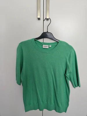 Grön stickad tröja från Kappahl - Snygg grön stickad tröja från Kappahl med rund halsringning och korta ärmar. Tröjan har en enkel och stilren design med ribbade kanter vid hals och nederkant. Perfekt för att addera lite färg till din outfit.