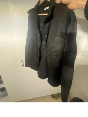 Svart overshirt från C.P. Company - Tjena Säljer en svart overshirt från C.P. Company väldigt bra skick förutom att på badgen så har ja råkat slå i den så lite av bokstaven är av men annars är den jätte fin! Hör av er om ni undrar något😊