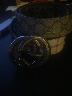  bälte med GG-mönster och silverfärgat spänne - Säljer ett bälte med klassiskt GG-mönster i beige och brunt. Bältet har ett stort, rundat silverfärgat spänne med G logga. Materialet är skinn och bältet har en elegant och tidlös design som sticker ut.