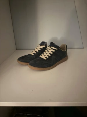Svarta sneakers med beige sula - Snygga svarta sneakers med beige gummisula och vita snören. Skorna har en klassisk låg profil och är tillverkade i ett material som ser ut som mocka eller nubuck. Insidan är ljusbeige och de har en stilren design som passar till många outfits.