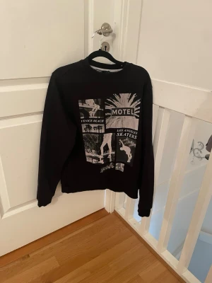 Svart sweatshirt med LA-skater - Cool svart sweatshirt med grafiskt tryck på framsidan med motiv från Los Angeles, Venice Beach och skaterkultur. Tröjan har rund hals och långa ärmar. Perfekt för dig som gillar streetstyle och skater-vibes.