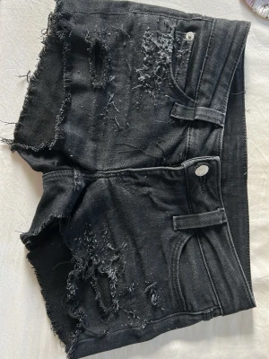 Svarta distressed shorts från Cheap Monday - Coola svarta jeansshorts från Cheap Monday med råa, fransiga kanter och slitna detaljer både fram och bak. Klassisk femficksdesign och knappstängning. Perfekta för dig som gillar en edgy och avslappnad stil. Jag har gjort dem själv 