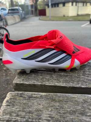Adidas Predator fotbollsskor röd/vit - Säljer ett par Adidas Predator fotbollsskor med en snygg kombination av rött, vitt och svart. Skorna har snörning och en innovativ design med greppvänlig sula och detaljer i neon. Perfekta för dig som vill dominera på planen!