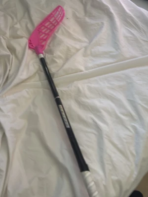 Innebandyklubba med rosa blad - Säljer en innebandyklubba med svart skaft och vitt grepp ifrån zone endast använt på 1-2 träningar . Bladet är i en stark rosa färg och har ett klassiskt nätmönster. Perfekt för dig som vill sticka ut på planen och gillar sportiga tillbehör.