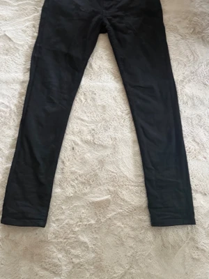 Nudie Jeans W30L30 svarta  - Säljer ett par svarta  jeans från Nudie Jeans med klassisk femficksdesign och broderad bakficka. Jeansen har smal passform och är tillverkade i stretchigt denim för en bekväm känsla. Perfekta för dig som gillar en stilren look.