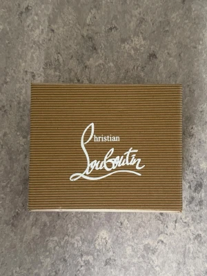 Christian Louboutin plånbok - Säljer en plånbok från Christian Louboutin med logga i svart och rött. Perfekt för att förvara eller skydda dina kort. Medföljer även care instructions.