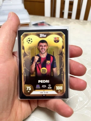 Match Attax Pedri samlarkort - Säljer ett Match Attax samlarkort från Topps med Pedri från FC Barcelona. Kortet har guldfärgad ram, klubbmärke och Champions League-symbol. Det är en 100 Club-kort med siffrorna 75 DEF och 100 ATT. Perfekt för dig som samlar fotbollskort!
