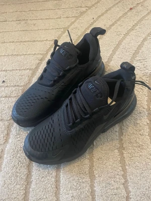 Nike Air Max 270 helsvarta sneakers - Säljer ett par HELT NYA helsvarta Nike Air Max 270 sneakers med mesh-överdel och synlig Air-enhet i hälen. Skorna har en sportig look med diskreta detaljer och klassisk Nike-logga på plösen. Perfekta för dig som gillar stilrena och bekväma sneakers. Köpta för 2000kr