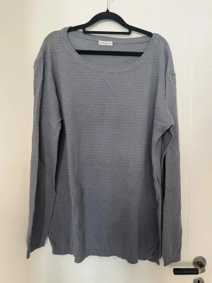 Grå stickad tröja med rund hals - En enkel och stilren grå stickad tröja från Jacqueline de Yong strl XL med rund halsringning och lång ärm. Tröjan har diskret strukturmönster och ribbade muddar vid ärmslut och nederkant. 
