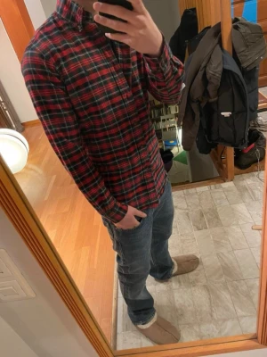 Röd Flannel Skjorta Polo Ralph Lauren - Klassisk röd och grön rutig skjorta från Polo Ralph Lauren i storlek XS, med knappar framtill och lång ärm. Skjortan har en normal passform och är tillverkad i mjuk bomull, perfekt för en avslappnad men ändå stilren look.