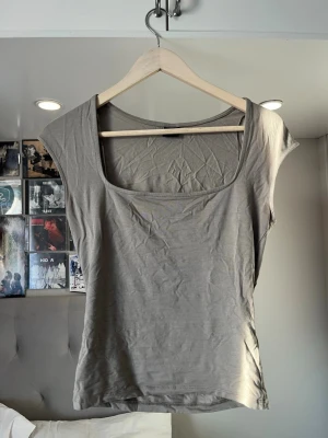 Beige topp med bred ringning Gina Tricot - Säljer en enkel och stilren beige topp från Gina Tricot. Toppen har bred ringning och är ärmlös med en figurnära passform. Perfekt att matcha med jeans eller kjol för en clean look.