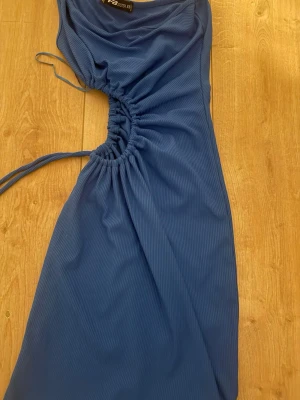 Blå oneshoulder klänning med snörning - Snygg blå oneshoulder klänning från PrettyLittleThing med cool snörningsdetalj i sidan som ger en unik look. Klänningen är figurnära och har ett mjukt, stretchigt material som känns bekvämt mot huden. Perfekt för dig som vill sticka ut.