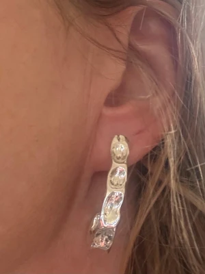 Silvriga chunky hoops örhängen - Säljer ett par silvriga chunky hoops med unik, vågig och organisk form. Örhängena är i metall med blank finish och har en modern, trendig look som sticker ut. Perfekta för dig som gillar statement-smycken och vill addera något extra till din stil.