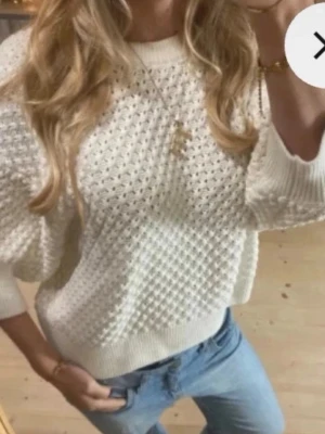 Vit stickad tröja med strukturmönster - Säljer en super härlig vit stickad tröja med snyggt strukturmönster och breda ribbade muddar vid ärmslut och nederkant. Tröjan har en avslappnad passform, rund halsringning och halvlånga ärmar. Perfekt att styla med jeans för en trendig look.
