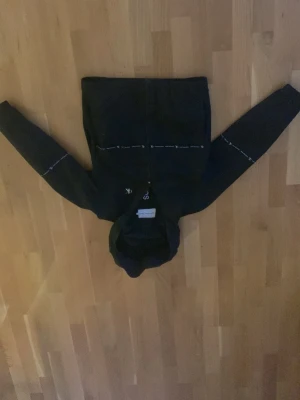 Svart vindjacka från Calvin Klein Jeans - Svart vindjacka med huva från Calvin Klein Jeans. Jackan har dragkedja framtill och vita logodetaljer på bröstet och ärmarna. Lätt och smidig modell som passar perfekt till streetwear-stilen.