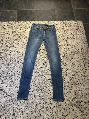 Blå slim fit jeans från tiger Sweden  - Säljer ett par klassiska blå slimfit  jeans från tiger Sweden med fem fickor och dragkedja. Jeansen har en snygg tvätt och kontrastsömmar, samt midjan. Perfekta för dig som gillar en slimmad passform och tidlös stil.