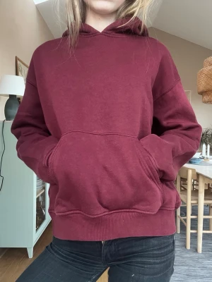 Vinröd hoodie från Gina Tricot - Mysig vinröd hoodie från Gina Tricot, modell basically basic. Klassisk passform med huva och stor känguruficka framtill. Tillverkad i mjukt bomullsmaterial och har ribbade muddar vid ärmslut och nederkant. Perfekt för en avslappnad och stilren look.