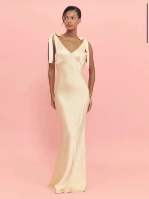 Balklännking i satin - Elegant långklänning i ljusgulfärgad satin med smickrande slim passform. Klänningen har v-ringad urringning, djup rygg och axelbandsdetaljer med knyt. Även dold dragkedja vid sidan. Perfekt för bal eller bröllop. Materialet ger en lyxig och glansig känsla. Såå fin verkligen 🥹😍💞 Storlek 36. Prislappar och ny skick. 