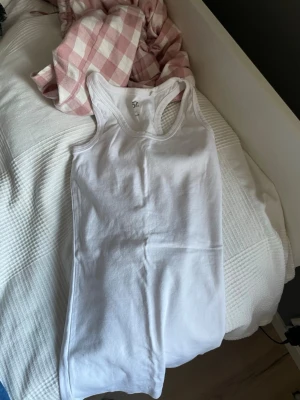 Vit linnetopp från 157, XS - Klassisk vit linnetopp från 157 i storlek XS. Tillverkad i 100% bomull med rund halsringning och ärmlös design. Perfekt att styla lager på lager eller bära som den är under varma dagar.