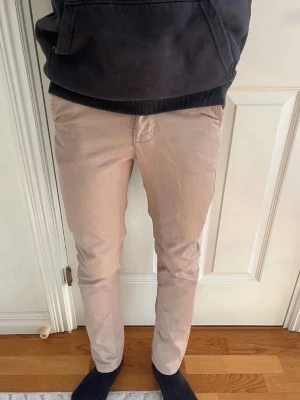 Beige chinos med smal passform - Snygga beige chinos med smal passform och klassisk design. Byxorna har två bakfickor med knappar och är tillverkade i ett mjukt bomullsmaterial som ger en skön känsla. Perfekta för en avslappnad men stilren look.
