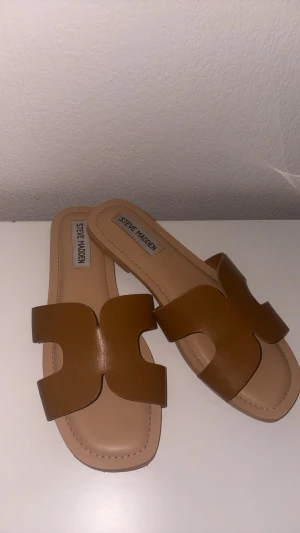 Bruna slip-in sandaler Steve Madden - Snygga bruna slip-in sandaler från Steve Madden med breda remmar i läderlook och öppen tå. Sandalerna har en stilren design med fyrkantig tå och ljus innersula. Perfekta för en trendig och avslappnad stil. Sandalerna är i storlek 38 och säljs för 400 kr hör av er vid funderingar 🌸använda ungefär 2 gånger 