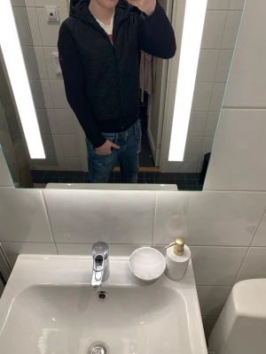 Svart quiltad cardigan j.lindberg  - Säljer en svart cardiganjacka ifrån j.lindberg med quiltat framstycke och huva. Ärmarna är ribbstickade och jackan har dragkedja framtill. Perfekt för lager på lager och ger en clean look till jeans eller chinos.