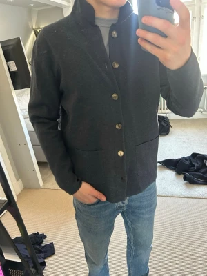 Mörkblå kofta från John Henric - Stilren mörkblå kofta från John Henric med knäppning framtill och två stora fickor. Koftan har hög krage och är tillverkad i mjukt material, perfekt för lager på lager. Nypris: 1049, mitt pris: 449