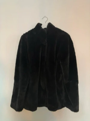 Svart pälsjacka från Mywear Woman - Snygg svart pälsjacka från Mywear Woman Outerwear Collection. Jackan har en klassisk rak passform, hög krage och är gjord i mjukt fuskpälsmaterial som ger en lyxig känsla. Perfekt för att hålla värmen under kalla dagar.