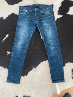 Blå slim fit jeans från Replay - Snygga blå slim fit jeans från Replay med klassisk femficksdesign. Jeansen har normal midja, dragkedjegylf och är tillverkade i stretchigt denimtyg för skön passform. Perfekta för en avslappnad och trendig look. W36 