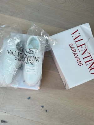 Valentino Garavani vita Rockstud sneakers - Säljer ett par vita Valentino Garavani Rockstud Untitled sneakers. Skorna har klassisk låg silhuett, vita nitar på sidorna och är tillverkade i slätt läder. Snygg och clean look med vita skosnören och diskret branding på plösen.