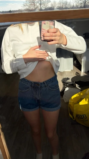 Mörkblå högmidjade jeansshorts - Säljer ett par mörkblå högmidjade jeansshorts med klassisk femficksdesign och uppvikta benslut. Perfekta till sommaren och lätta att matcha med olika toppar. Inga synliga detaljer som sticker ut, bara en clean och tidlös look.