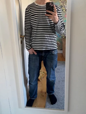 Randig långärmad tröja från Makia - Säljer en svartvit randig långärmad topp från Makia. Tröjan har rund halsringning och en liten bröstficka på vänster sida. Tillverkad i mjuk bomull för en skön och avslappnad look. 