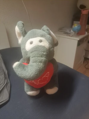 Gosedjur elefant med hjärta - Söt grå elefant i plysch som håller ett rött hjärta med broderade vita detaljer. Elefanten har vita inslag på öron, fötter och runt ögonen. Perfekt som present eller dekoration i rummet.