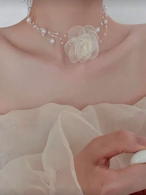Halsband Necklace Choker med pärlor och tygblomma - Romantisk choker i cremevitt med flera rader små och stora pärlor samt en stor tygblomma i mitten. Halsbandet har en luftig och elegant design med transparenta trådar och en mjuk, feminin känsla. Perfekt för dig som gillar unika accessoarer med blommiga detaljer.