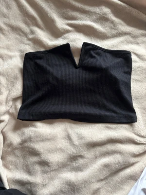 Svart ärmlös cropped topp S – V-ringad - Svart ärmlös cropped topp med V-ringad slits mellan brösten 🤍  Toppen sitter tight och håller sig på plats utan problem. Perfekt för fest eller kvällsoutfits.  Storlek S. Jag är 170 cm och brukar ha storlek S/M – toppen passar mig fint ✨  Nästan aldrig använd och i mycket bra skick. Saknar märke, köpt från en kompis. En enkel men trendig topp som lyfter en outfit.