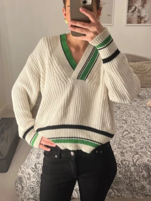 Vit stickad tröja Gina Tricot XS - Säljer en vit stickad tröja från Gina Tricot i storlek XS. Tröjan har gröna och svarta ränder vid v-ringningen, ärmsluten och nederkanten. Oversized passform och ribbstickad struktur.