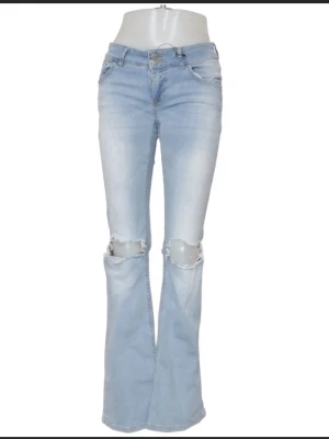 Ljusblå bootcut jeans med slitningar - Säljer ett par ljusblå bootcut jeans med slitna knän och klassisk femficksmodell. Jeansen har hög midja och utsvängda ben, vilket ger en retro och trendig vibe. Perfekta för dig som gillar en avslappnad men ändå stilsäker look.
