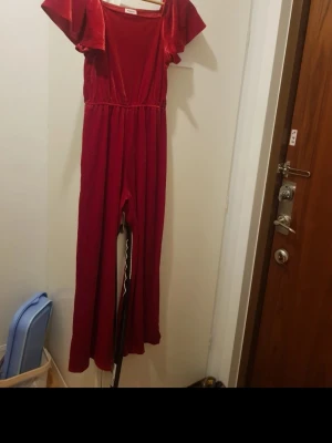 Röd jumpsuit med vida ärmar - Snygg röd jumpsuit med korta, vida ärmar och rund halsringning. Jumpsuiten har resår i midjan för en skön passform och långa, raka ben. Perfekt för dig som vill sticka ut med en färgstark och trendig look. Storlek 158/164