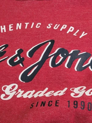 Röd hoodie från Jack & Jones - Snygg röd hoodie från Jack & Jones med tryck framtill i vitt och svart. Klassisk modell med huva och långa ärmar. Tillverkad i mjukt bomullsmaterial som är skönt att ha på sig. Perfekt för en avslappnad och trendig stil.