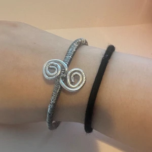 Silvrigt armband med spiraldesign - Unikt armband i silverfärgad metall med en cool spiralformad detalj framtill. Armbandet har en lindad trådlook som ger en modern och edgy känsla. Perfekt för dig som gillar statement-smycken och vill sticka ut lite extra.
