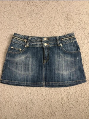 Y2k vintage kjol - Snygg blå jeanskjol i kort modell med dubbla knappar framtill, dragkedjedetalj vid linningen och klassiska fickor både fram och bak. Kjolen har slitna partier för en cool look och passar perfekt till en avslappnad stil. Passar er mes s-xs skulle jag sägs 