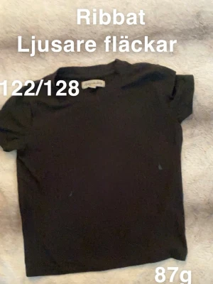Svart ribbad t-shirt  - En svart ribbad t-shirt med korta ärmar och rund hals. Enkel och stilren modell som passar till det mesta. Perfekt för dig som gillar basic men ändå vill ha lite struktur.🌸 Ljusare fläckar. Ribbat. Storlek 122/128