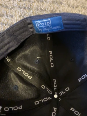 Marinblå keps från Polo Ralph Lauren - Snygg marinblå keps från Polo Ralph Lauren med klassisk böjd skärm och vit broderad logga framtill. Kepsen är helt ny men behöver sälja pågrund av att den inte passar. Skriv om ni vill diskutera pris!