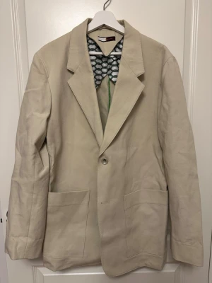 Beige kavaj från Tommy Hilfiger - Beige Tommy Hilfiger kavaj, strl 50. 100% Bomull. Ärmlängd (cm) 69 , Axelbredd (cm) 54.