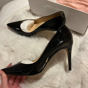 Svarta lackpumps med spetsig tå - Snygga svarta pumps i lack med spetsig tå och hög klack. Skorna har en elegant och klassisk form som ger en stilren vibe. Insidan är beige och sulan är ljus. Perfekt för dig som gillar att sticka ut med en chic look.