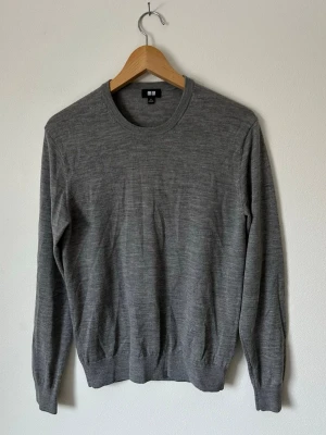 Grå stickad tröja från Uniqlo - En stilren grå stickad tröja från Uniqlo i mjuk ullblandning. Tröjan har rund halsringning, långa ärmar och ribbade muddar vid ärmslut och nederkant. Perfekt basplagg för lager på lager och enkel att matcha. 8A10